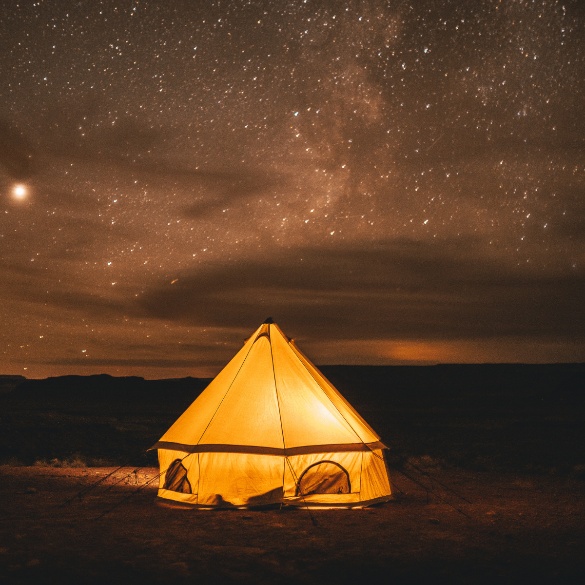 Beige 10' Regatta Bell Tent with lights inside glowing under the starry sky at night
