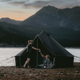 10 regatta bell tent night sky in front of lake with two women sharing a drink