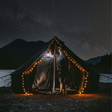 10 Regatta Bell Tent Nigh Sky placed under starry sky with fairy lights on the entrance and woman holding lantern in front of it