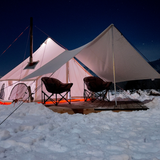 avalon bell tent set up in the snow on a platform with awning in front and chairs under it