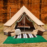 Beige 10' Regatta Bell Tent set up in front of stone wall decorated with leaves and light bulbs and carpets with a bed inside