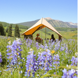 Rover scout tent placed in flowers field with front and back walls rolled, side mesh closed and a couple enjoying their drinks together 