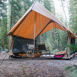 Rover scout tent placed in the forest with its front and back mesh rolled and a white husky dog laying on a dog bed with a chair and table next to it