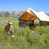 Rover scout tent placed in the grass among flowers while a woman picks the flowers sitting in front of the tent