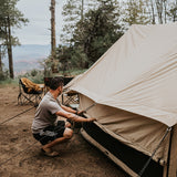 Rover scout tent placed in the forest while a man rolls up the sides to reveal the mesh inside