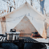 alpha wall tent in the snow blurred in the background with a bbq grill in focus