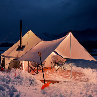 avalon bell tent set up in the snow with lights glowing inside and a camping stove chimney coming out of the hot tent stove jack