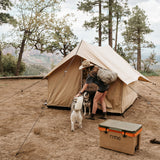 Adventurous woman setting up a scout tent in a rustic outdoor setting with two dogs